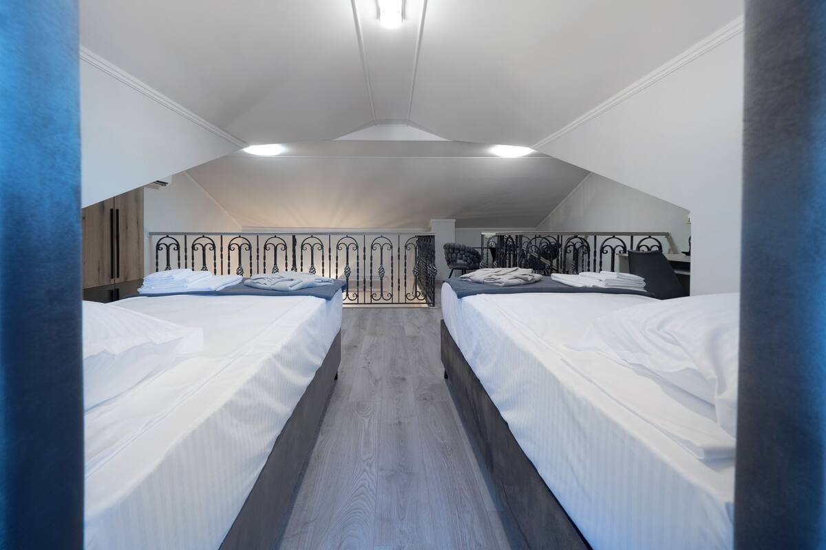 Quarto com duas camas, piso de madeira e teto inclinado com claraboia.