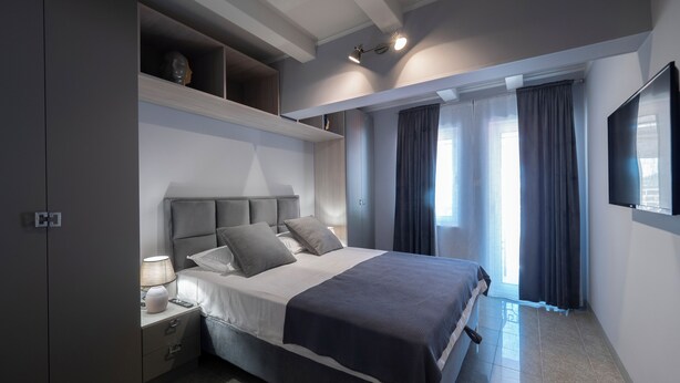 Een moderne slaapkamer met een groot bed, inbouwkasten, een nachtkastje en een aan de muur bevestigde televisie.