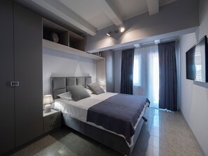 A modern bedroom with a large bed, built-in shelving, a bedside table, and a TV mounted on the wall. - Apartments Cataleya Przno (Pržno)