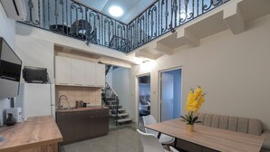 Een moderne keuken met een houten aanrechtblad, witte kasten en een ingebouwde kookplaat. Er is een eethoek met een houten tafel en witte stoelen. Een trap met een zwarte leuning leidt naar een verdieping.