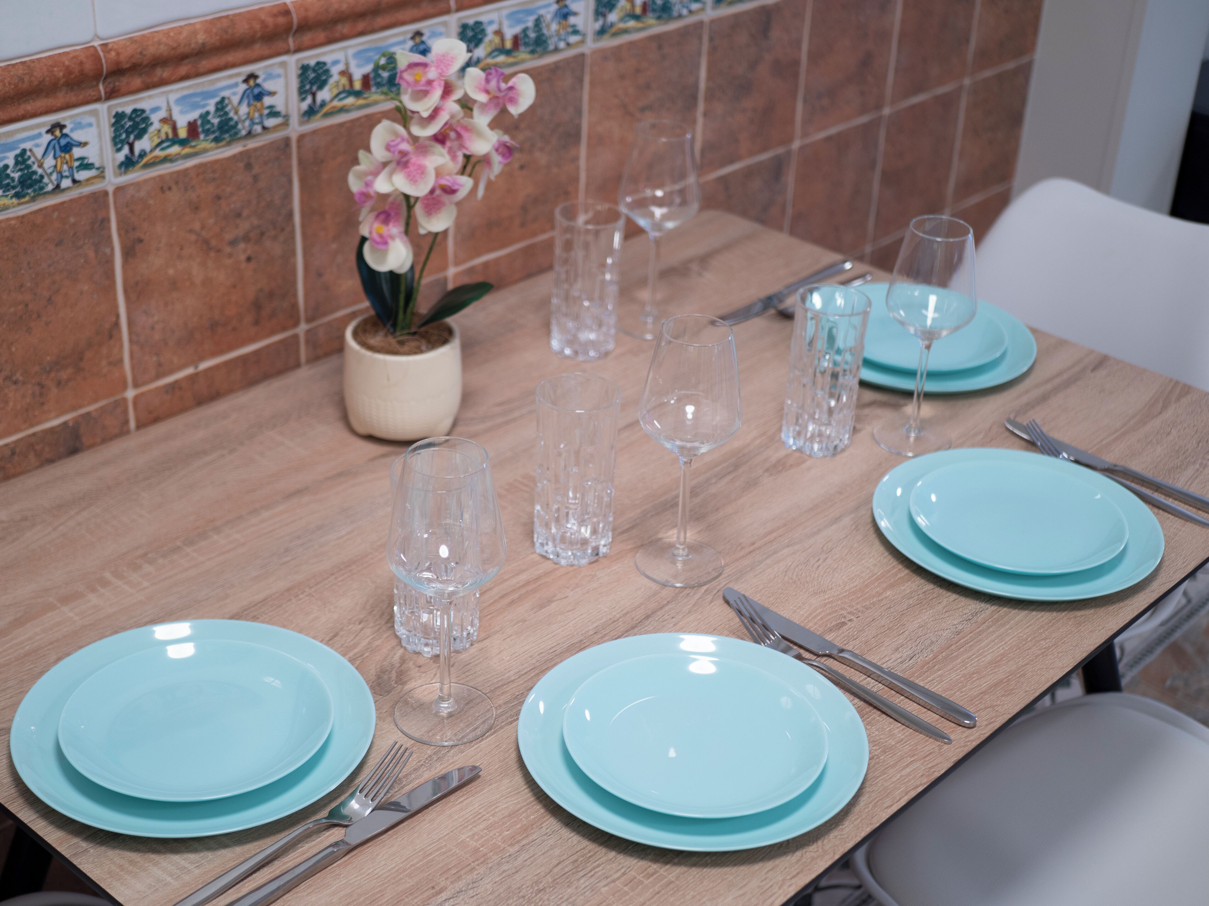 A dining table set with blue plates, clear glasses, and cutlery.