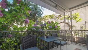Een terras buiten, met een tafel en twee stoelen, omgeven door een metalen hek en weelderige begroeiing.