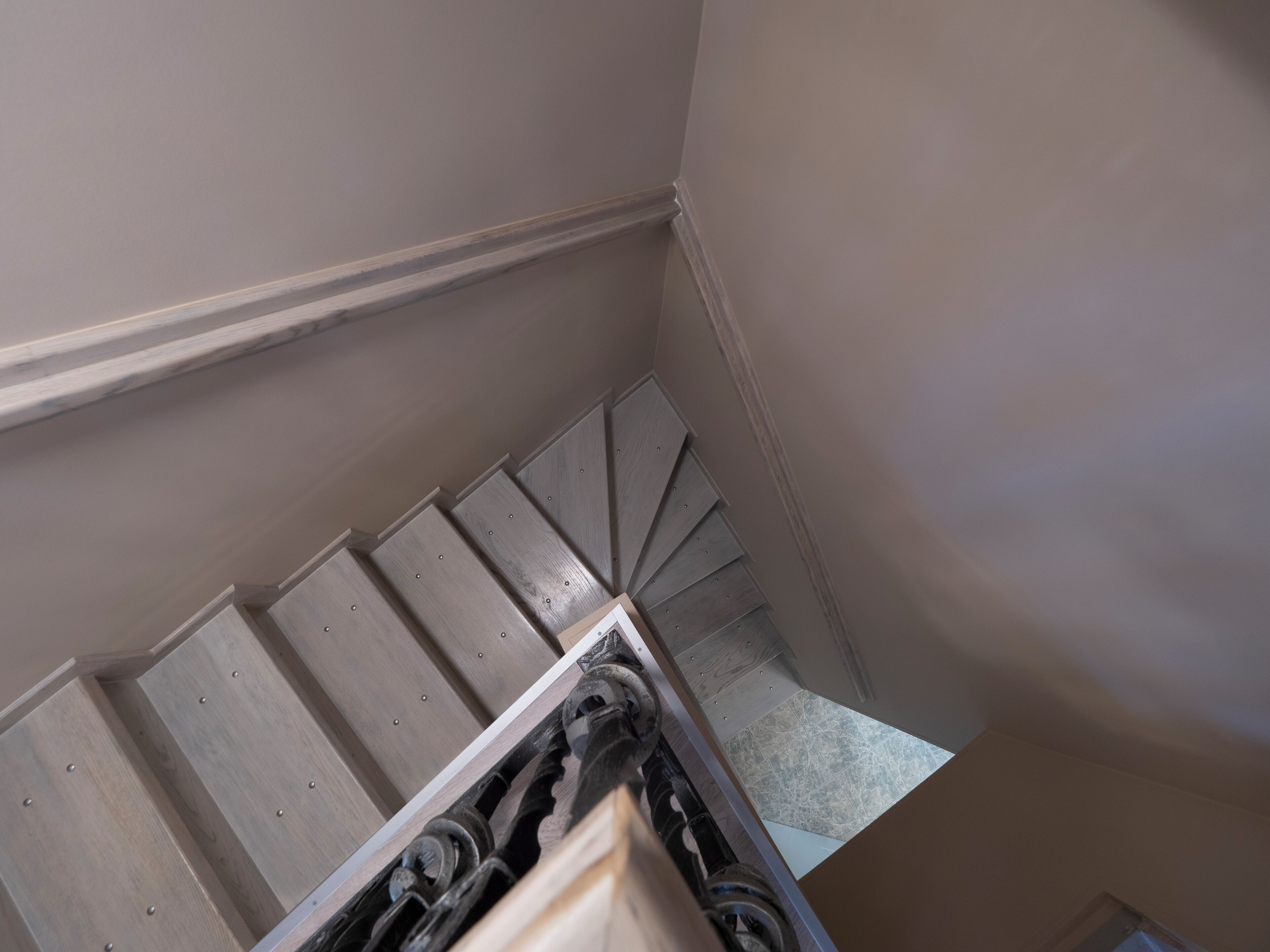 A view of a wooden staircase with a handrail, leading to a landing with a tiled floor.