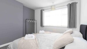 Quarto moderno com cama, radiador, janela com cortinas e um suporte de toalhas na parede.