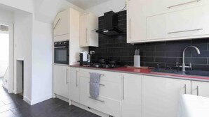 Uma cozinha moderna com armários brancos, painel de azulejos pretos, uma pia de aço inoxidável e bancada vermelha.
