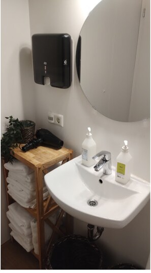 A bathroom with a white sink, two bottles of hand soap, a black telephone, a basket with a plant, and a wooden shelf with folded towels. - Buubble Hotel-Ölvisholt (Selfoss)
