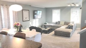 A modern living room with a dining area, grey walls, a mounted TV, and a staircase. - 5 Bedroom Home, 13 mins away from Skyline Drive (Waynesboro)