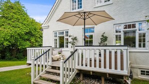 A white house with a wooden deck, a beige umbrella, and a white railing. - Beautiful Villa, 150 m2 activity hall with tabletennis etc. outdoor 6 pers. spa (Taastrup)