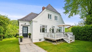 A two-story house with a white exterior, a tiled roof, and a front porch with a railing. - Beautiful Villa, 150 m2 activity hall with tabletennis etc. outdoor 6 pers. spa (Taastrup)