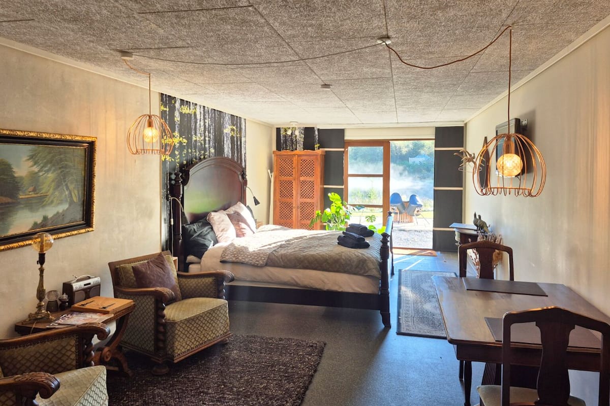 Ein Schlafzimmer mit Bett, Stuhl, Tisch und einem Bild an der Wand.