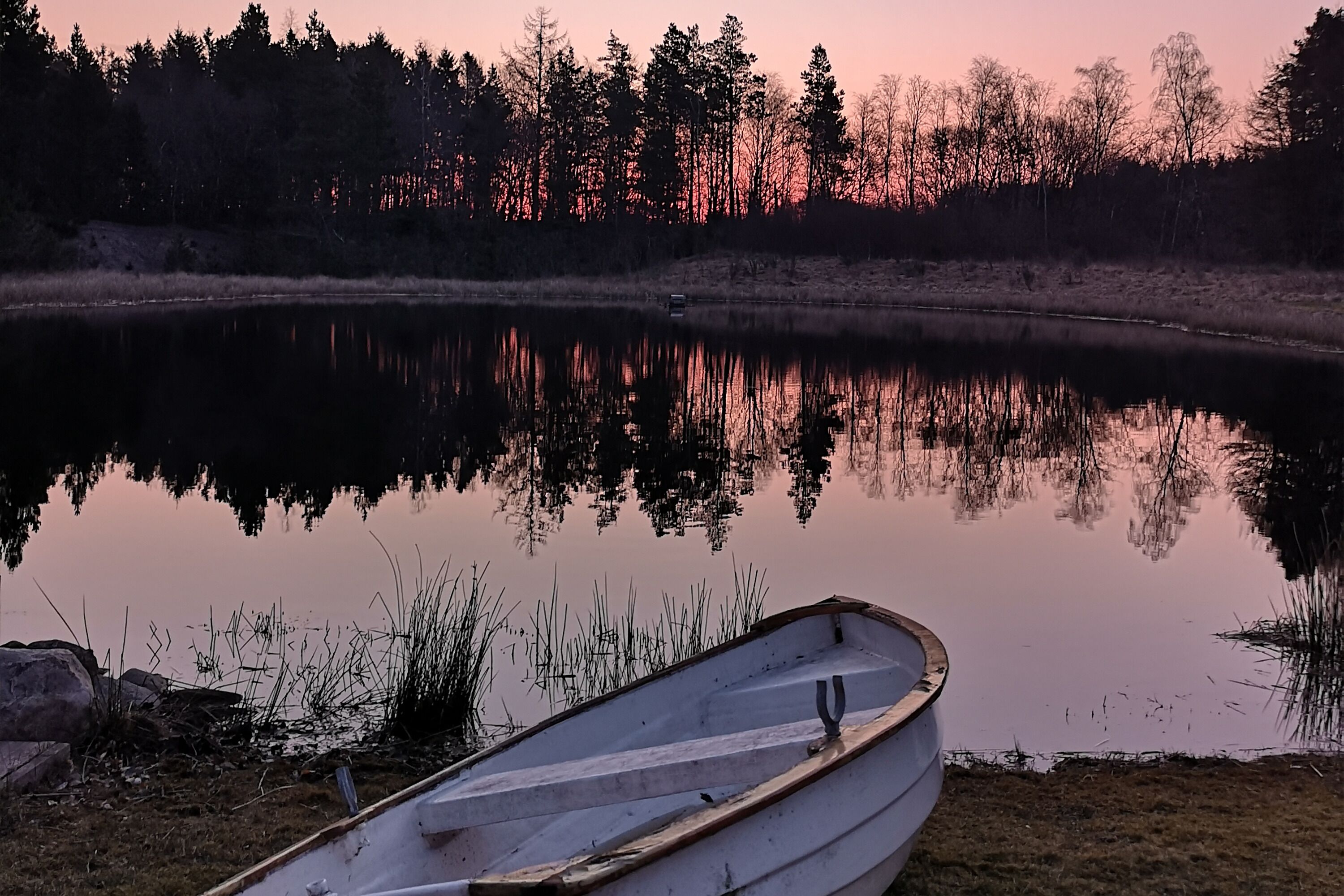 Un lago calmo al tramonto con una barca a remi in primo piano.