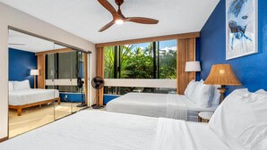 Habitación de hotel con dos camas, ventilador de techo, ventanas amplias y vistas al exterior con vegetación.