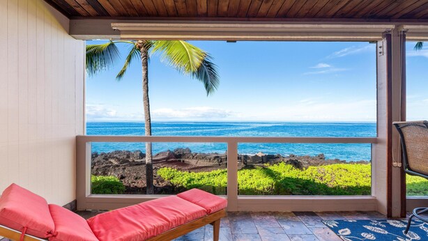 Un balcón con una silla acolchada roja, vista al océano y paisaje tropical.