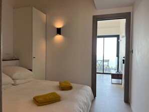 A bedroom with a bed, two towels, a bedside table, and a view of a balcony.
