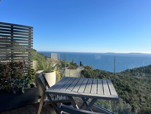 A wooden deck with a table and chairs, overlooking a coastal landscape.