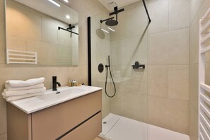 A modern bathroom with a white vanity, a glass shower enclosure, and a white towel stack.