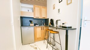 A compact kitchen with wooden cabinets, a built-in oven, a coffee maker, and two stools.