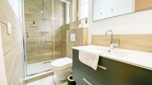 A modern bathroom with a glass-enclosed shower, a toilet, a sink with a towel, and a mirror.