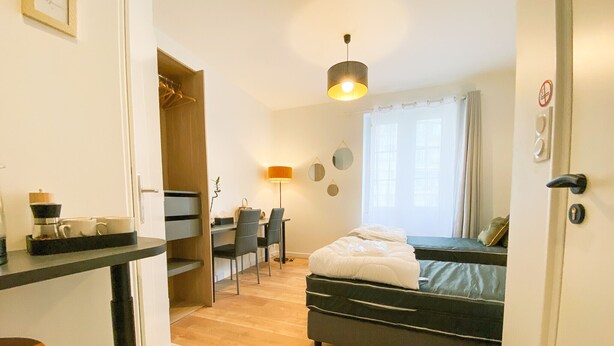 A compact hotel room with a bed, a desk, a chair, a lamp, and a window with curtains.