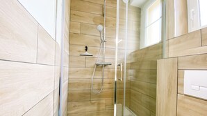 A modern shower with a glass door, wooden panel walls, and a visible control panel.