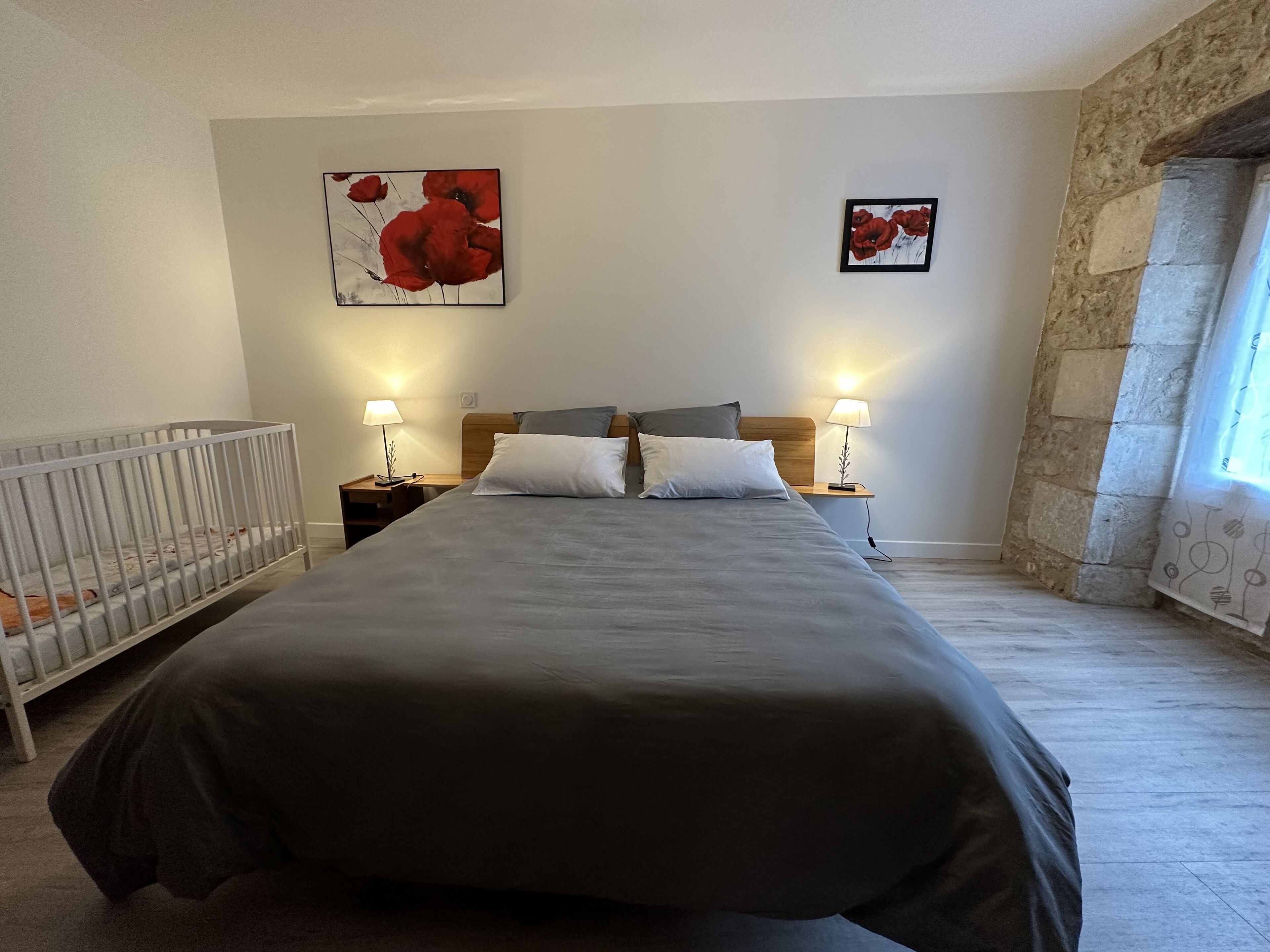 A bedroom with a large bed, two bedside tables with lamps, a crib, and two framed pictures on the wall.