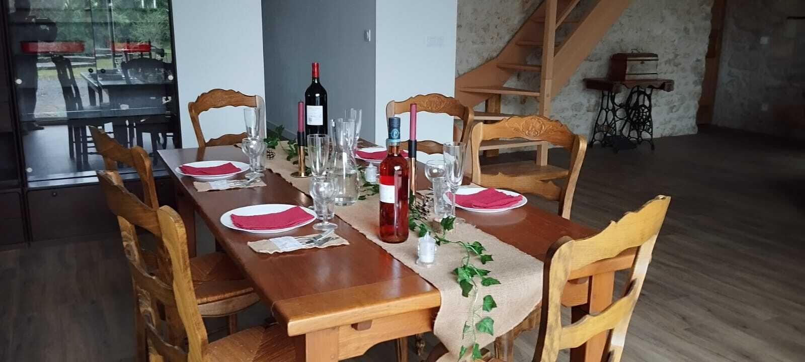 Un tavolo da pranzo apparecchiato con piatti, bicchieri e una bottiglia di vino, circondato da sedie in legno.