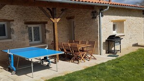 A stone building with a table tennis table and chairs, a barbecue grill, and a small window.