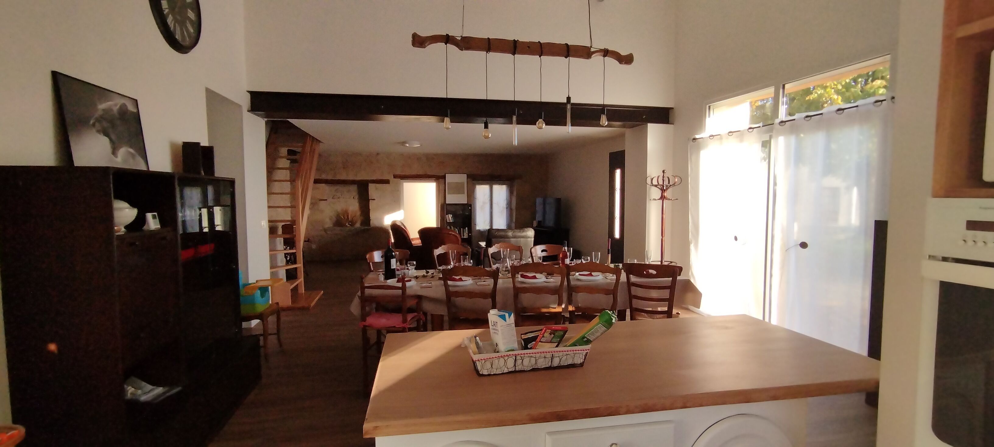 A spacious living area with a dining table set for four, a kitchen area with a refrigerator, and a staircase leading to an upper level.