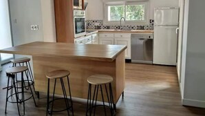 A modern kitchen with a central island, bar stools, white cabinetry, and a window providing natural light.