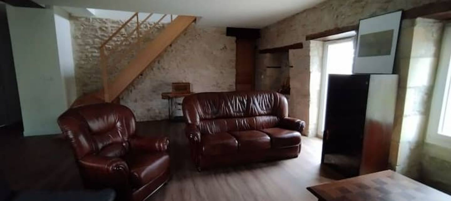 Een woonkamer met een bruine leren bank, een houten salontafel en een televisie.