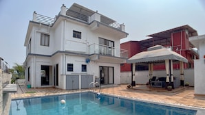 Una moderna casa a due piani con piscina, un'area salotto esterna coperta e un balcone.