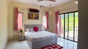 Una camera da letto con un letto, un comodino, una finestra, una ventola a soffitto e vista su spazi verdi.