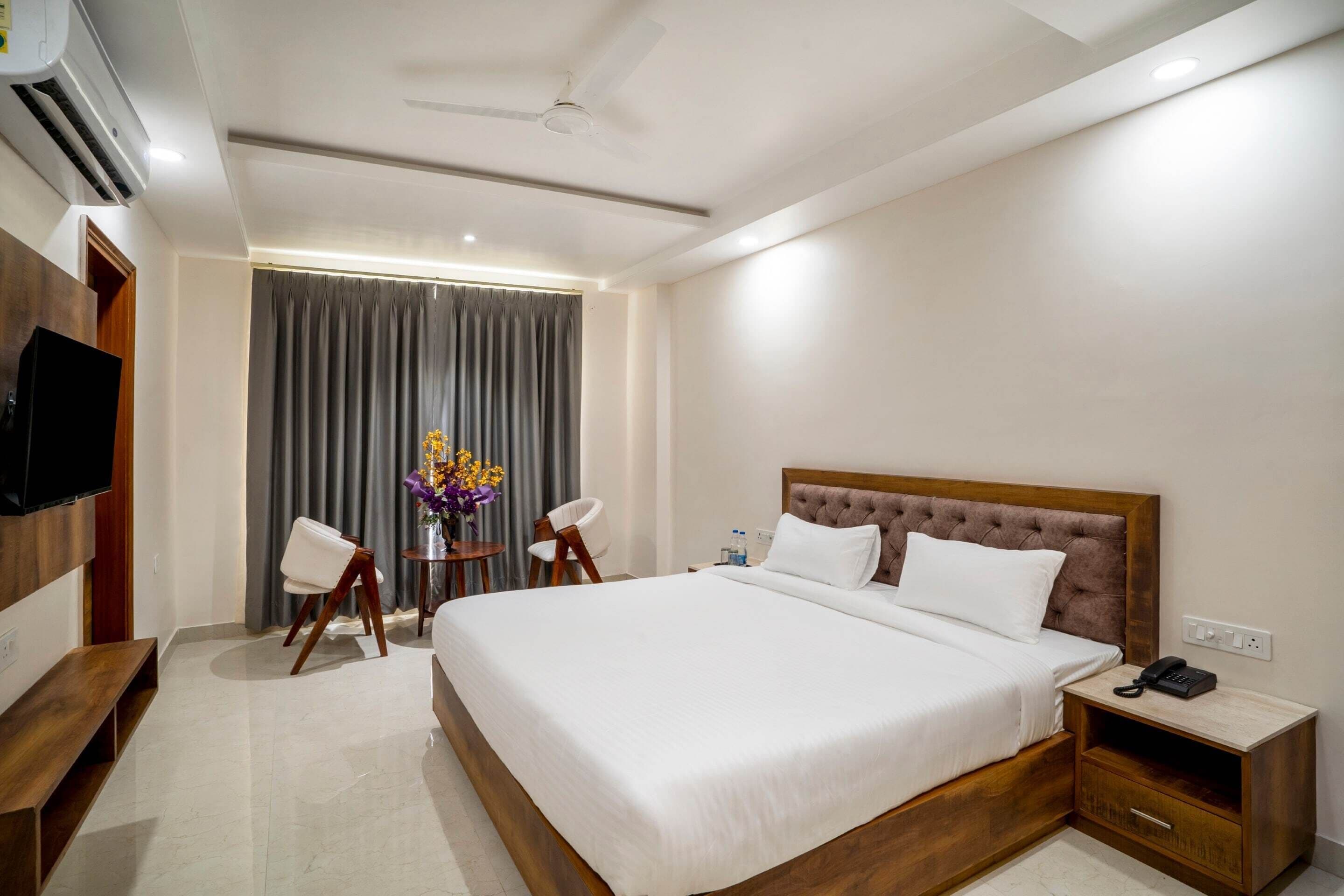 A hotel room with a large bed, bedside table, TV, and a ceiling fan.