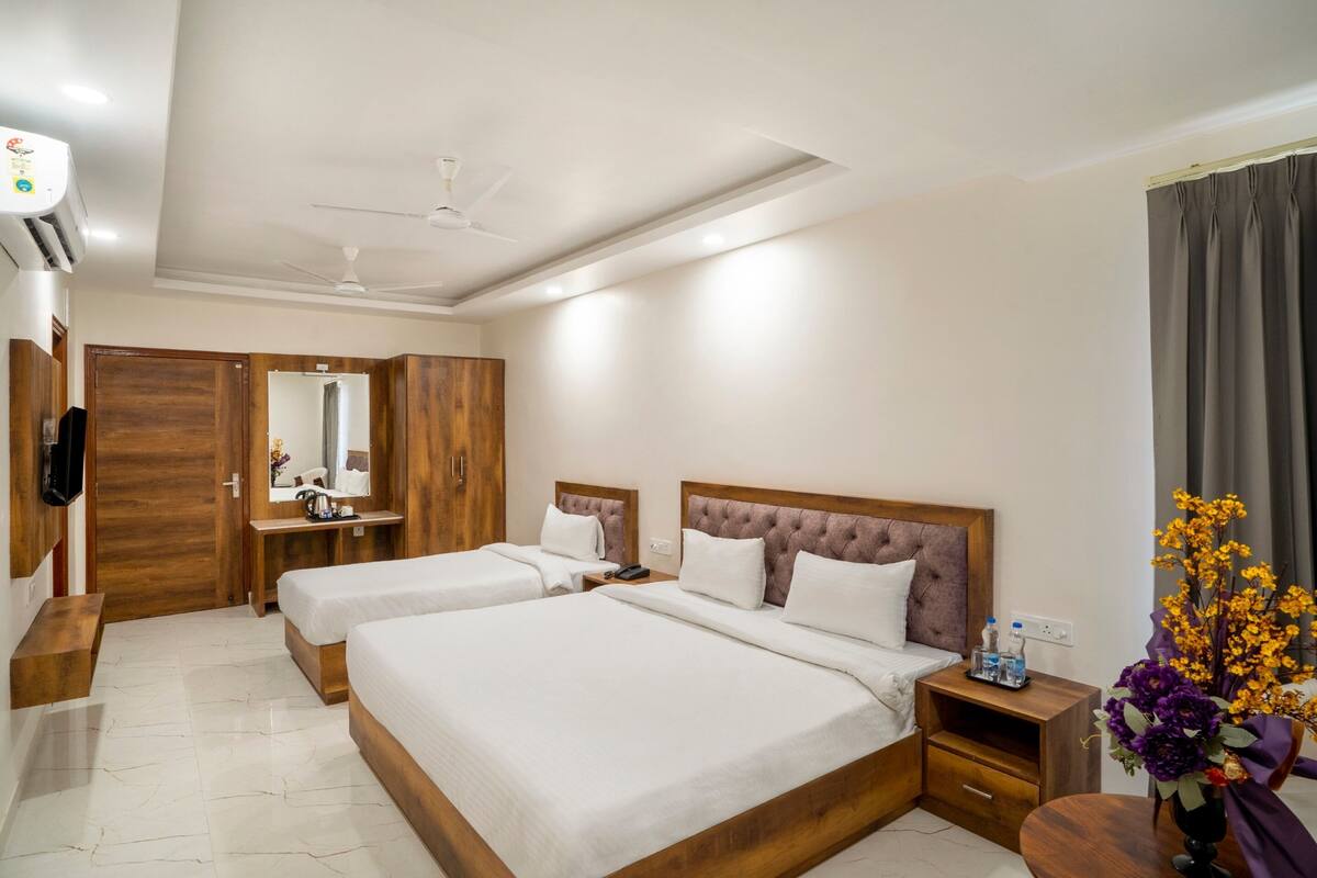 Habitación de hotel con dos camas, un tocador con espejo, un ventilador de techo y una mesita de noche con un florero.