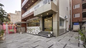 A modern building with a glass entrance, potted plants, and a tiled courtyard. - Hotel La Mirage (Noida)