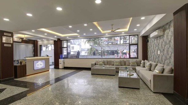 A modern lobby with a reception desk, a seating area with sofas, and large windows offering a view of the outside. - Hotel La Mirage (Noida)