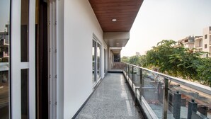 A narrow balcony with a wooden ceiling, glass railings, and a view of a cityscape. - Hotel La Mirage (Noida)