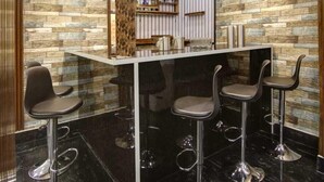 A modern bar area with a reflective surface, black marble flooring, and four bar stools. - Hotel La Mirage (Noida)