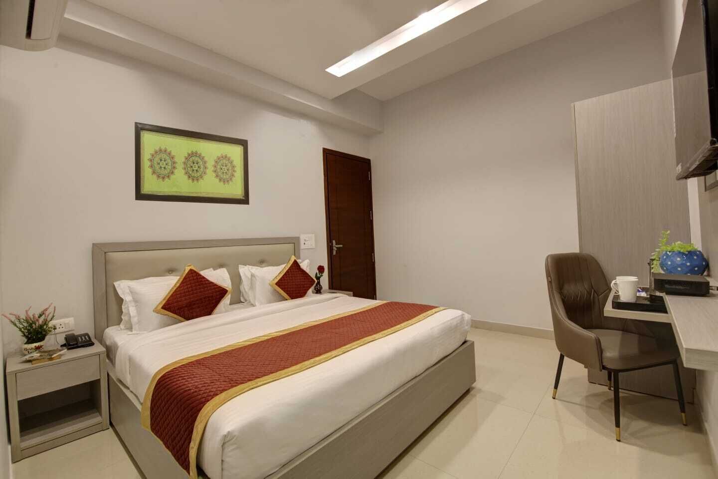 A hotel room with a bed, a desk, a chair, a small table, a wall-mounted TV, and a door.