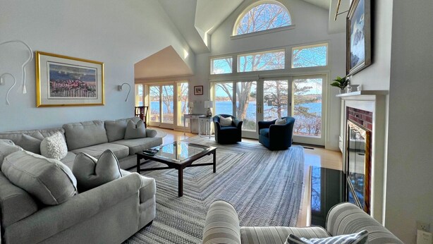 A spacious living room with a high ceiling, large windows, and a fireplace. - Pet Friendly Spacious Waterfront Home With A Deep Water Access Dock (2324) (Cotuit)