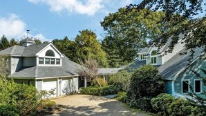 A two-story house with a garage, surrounded by dense greenery and trees. - Pet Friendly Spacious Waterfront Home With A Deep Water Access Dock (2324) (Cotuit)