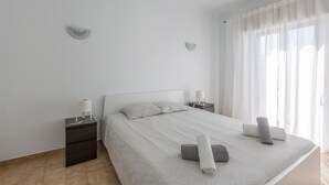 Une chambre moderne avec un grand lit, deux tables de chevet et une fenêtre ornée de rideaux légers.