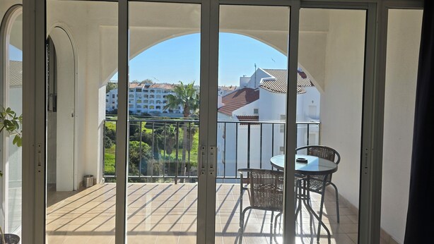 Un balcon avec une table et des chaises, un pot de fleurs et une vue sur des immeubles et de la verdure.