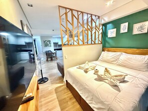 A hotel room with a bed, a desk, a fan, and a view of the kitchen and dining area. - Seme 1br  at abreezaplace towers ! With WIFI   with partition (Davao City)