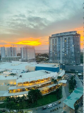 A high-rise building with a curved glass facade, surrounded by other buildings and a parking area.