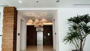 Eine moderne Lobby mit einer großen Topfpflanze, einer Holz-Akzentwand und einem Schild für den Aufzug 2.