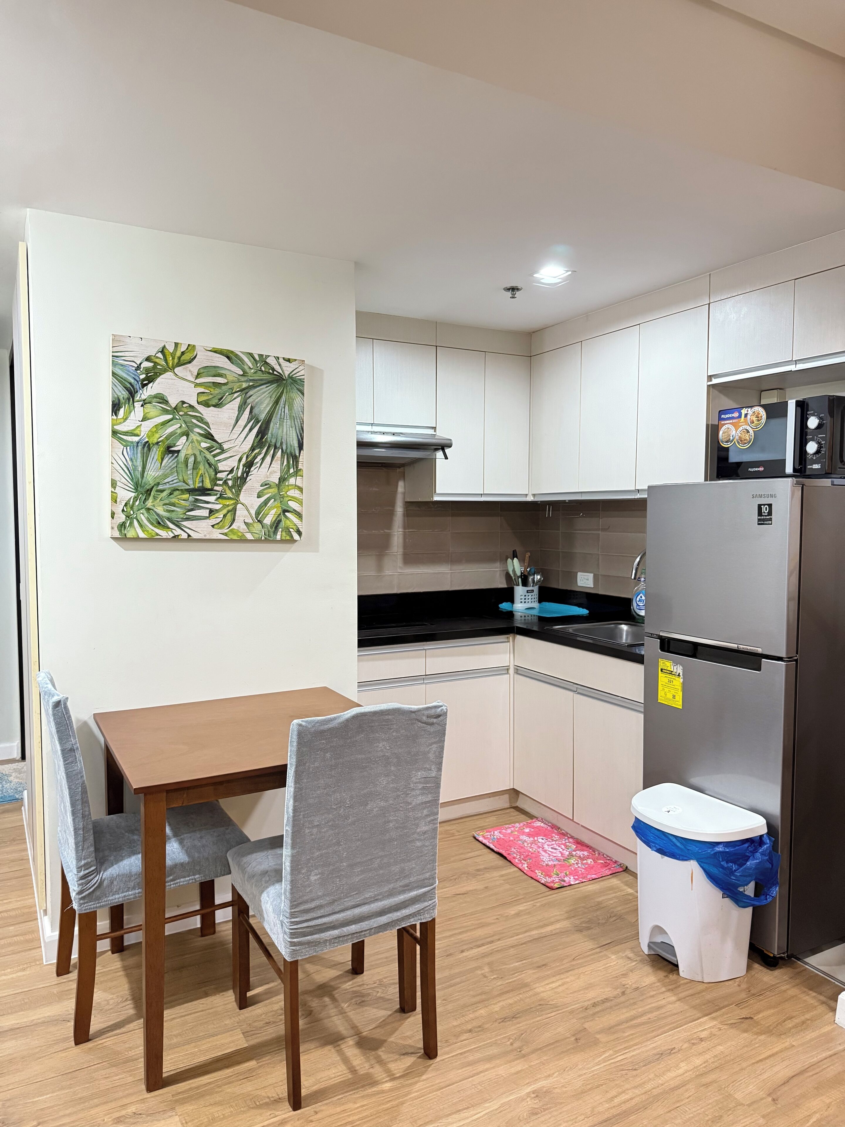 A compact kitchen with a dining table and chairs, a refrigerator, and a microwave.