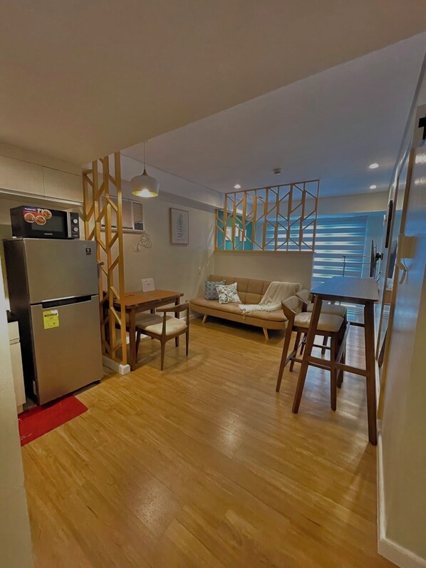A compact living space with a kitchenette, a sofa, a dining table, and a wooden partition.