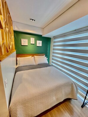 A bedroom with a bed, green walls, and a window with blinds.