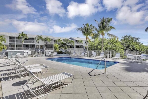 A pool area with lounge chairs, a swimming pool, and a building with balconies and palm trees.